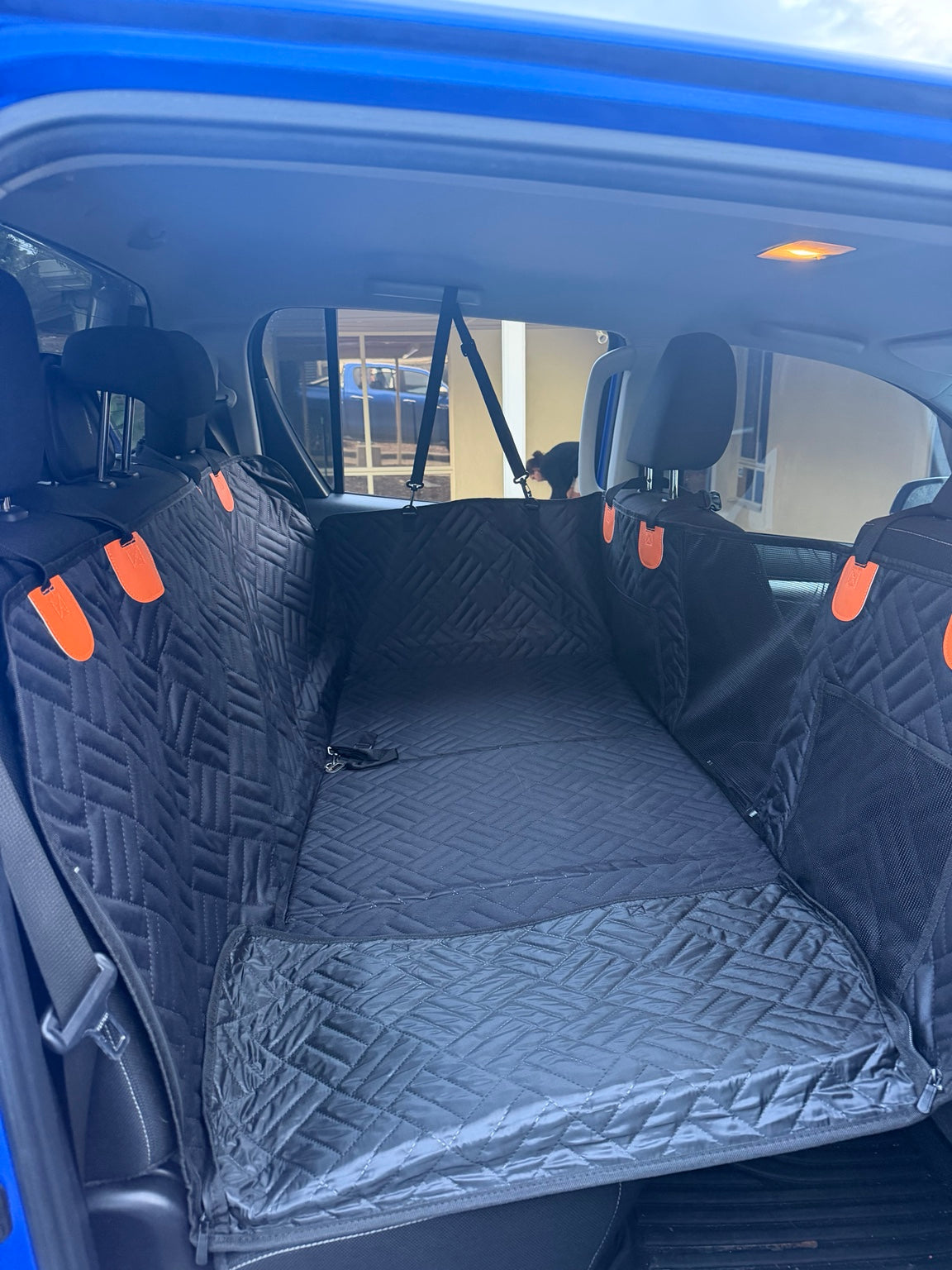 Wagvora Back Seat Extender installed across the rear seat of a dual-cab ute, with the quilted hard-bottom platform bridging the footwell and orange attachment tabs on the side panels